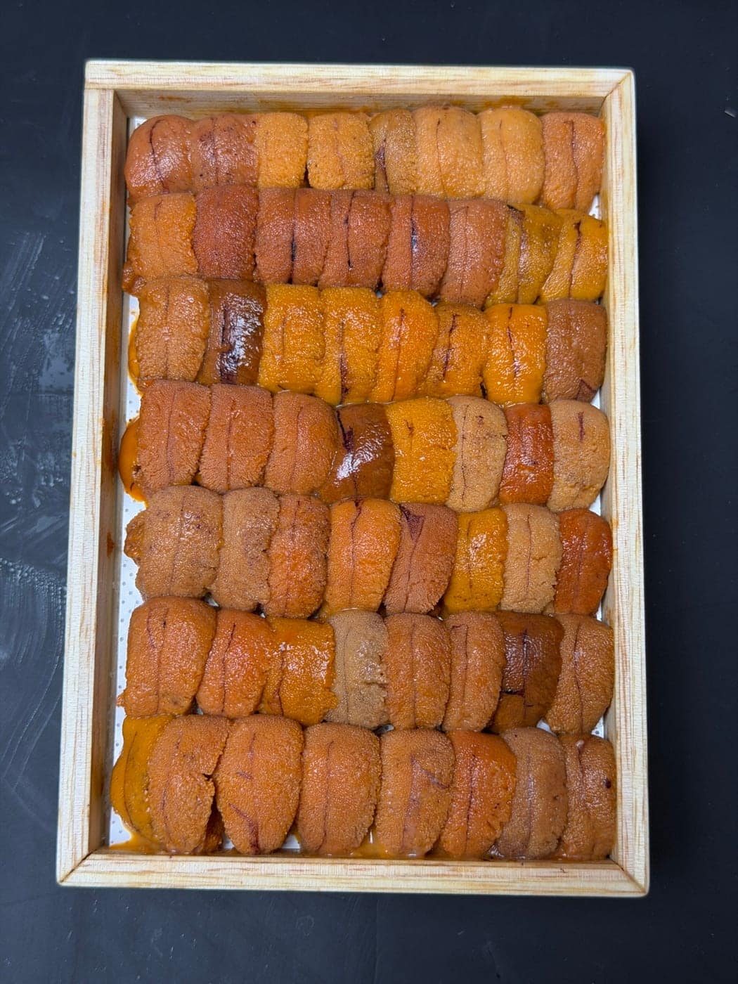 A wooden tray of Hokkaido uni, lobes graded by colour, on a dark counter